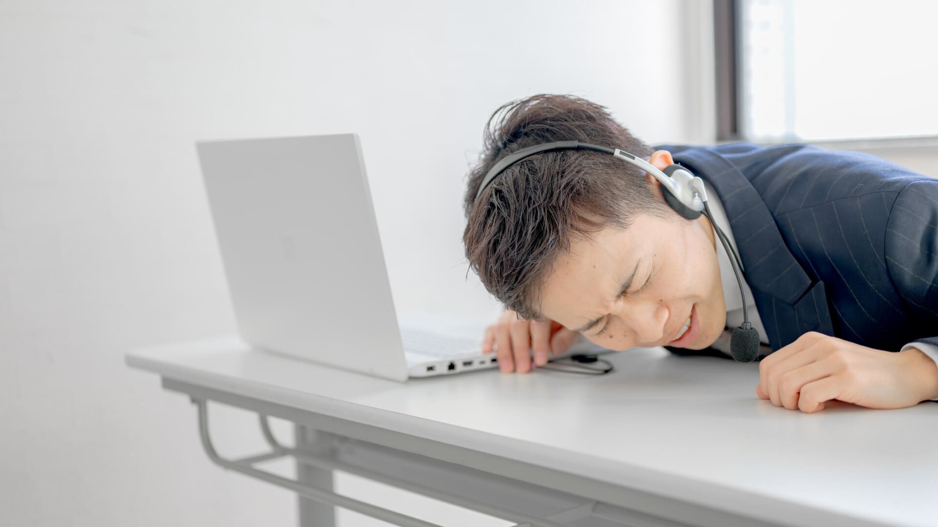 机でうなだれるヘッドセットを付けた男性